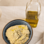 Creamy homemade air fryer baba ganoush in a rustic bowl, topped with olive oil and parsley, served with olive oil on a neutral linen background.